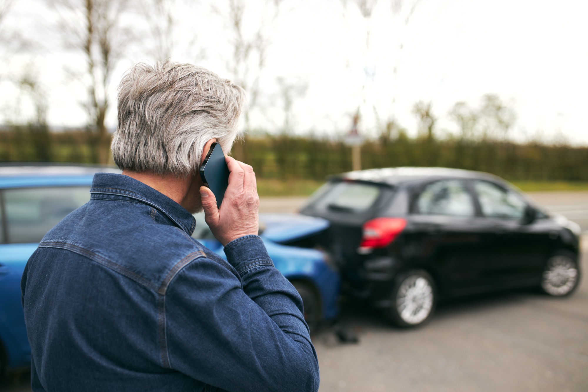 Rear View Of Senior Male Driver Calls Car Insurance Company On Mobile Phone After Traffic Accident