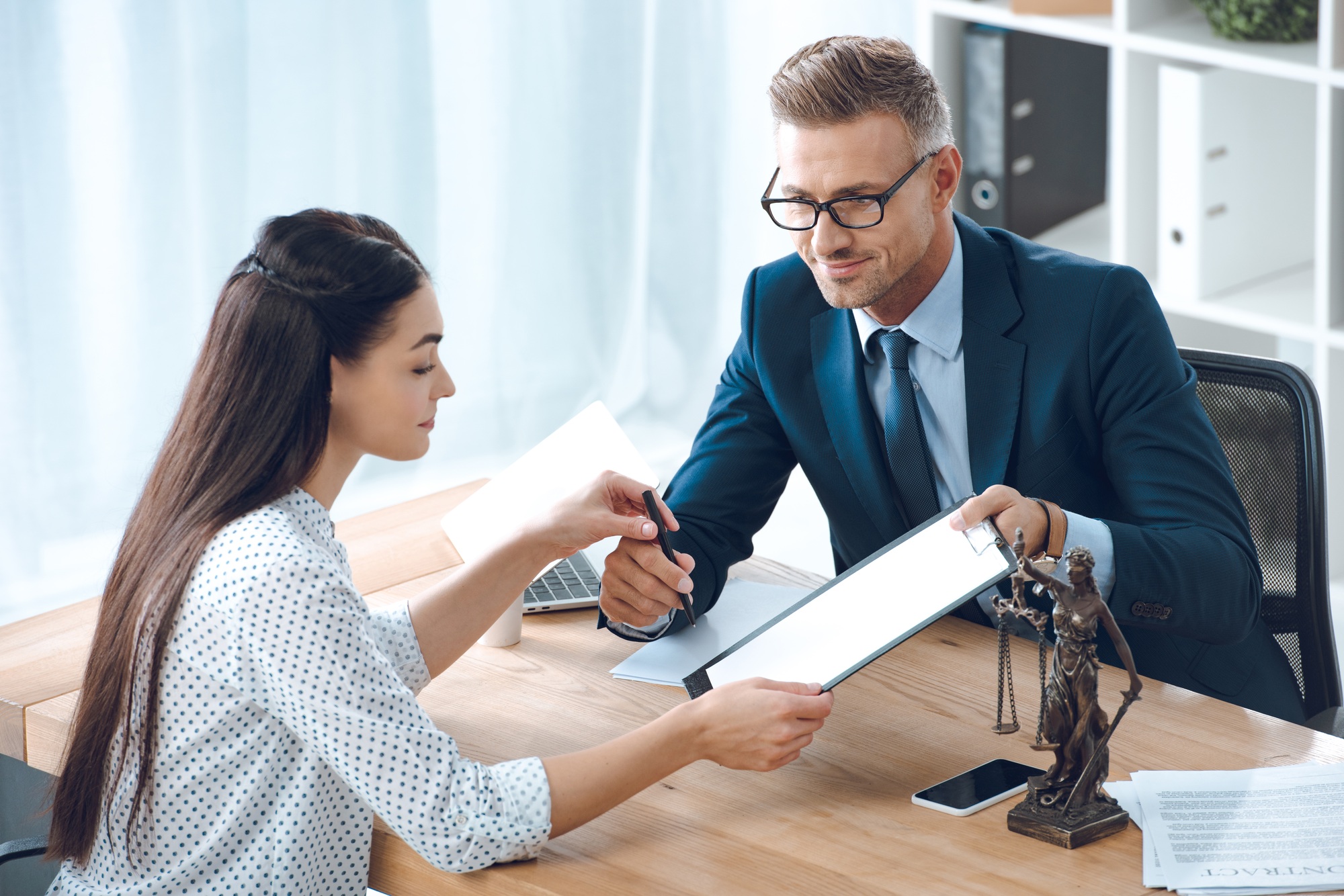 smiling lawyer giving clipboard and pen to young woman in office