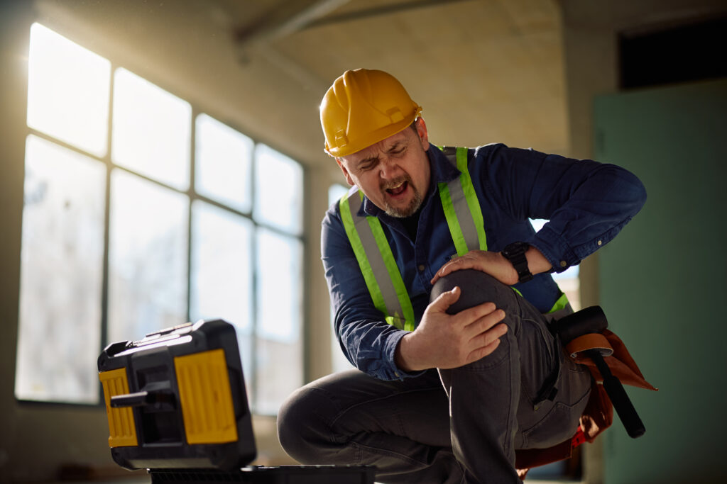Mature construction worker with injured knee at building site.
